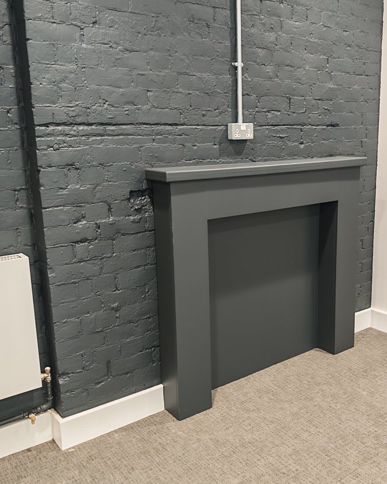 Painted grey fire surround against a dark brick wall