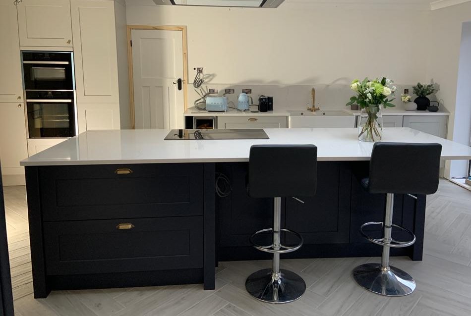 Kitchen with a navy shaker island, white quartz worktop and brass handles