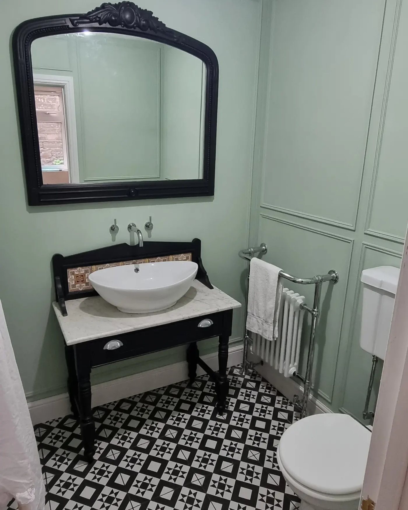 Sage green bathroom with panelled walls and a black washstand