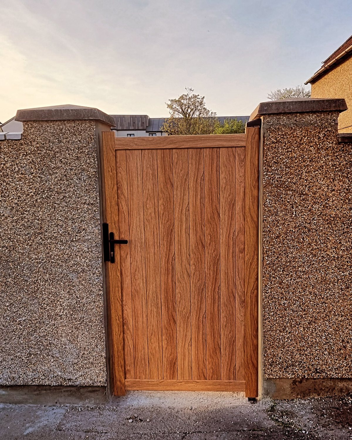 Wood-effect garden gate fitted between two pebble-dashed pillars